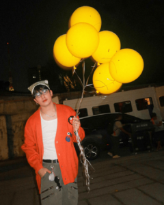 Maki Filipino singer wearing orange cardigan over sando and beanie with yellow balloons